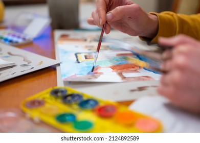 Closeup Of Watercolor Painting Process. Brush In Hand Above Painting. Colorful Medieval City Street On Paper Board.