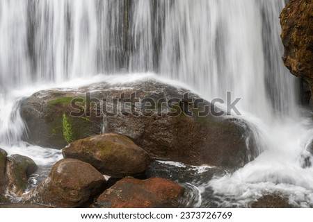 Closeup of a waterfall splashing on a large rock. Whatcom Falls cascading down onto a huge boulder at the base of the waterfall with some backsplash.