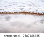 A close-up of waves crashing onto a sandy beach, highlighting the foam and air bubbles on the wet sand.