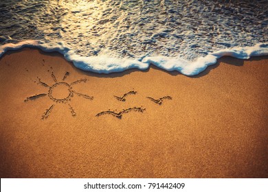 Closeup waves, sun and birds drawing on the sand beach near the ocean.