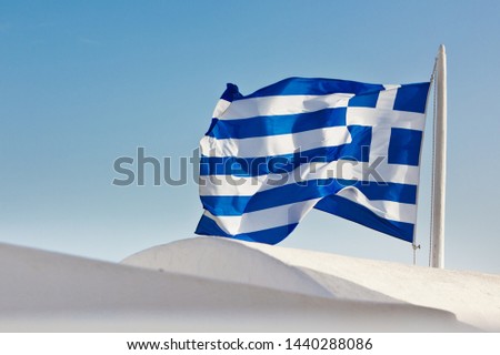 Close-up of a waving flag of Greece over the white round roofs of Santorini, Greece
