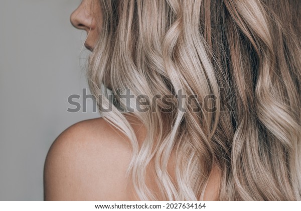 Close-up of the wavy blonde hair of a young\
blonde woman isolated on a gray background. Result of coloring,\
highlighting, perming. Beauty and\
fashion