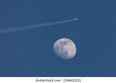 Closeup of the waxing moon and an airplane passing close by, leaving a contrail  - early evening capture against dark blue sky. Stuttgart, Germany April, 13, 2022 - Powered by Shutterstock