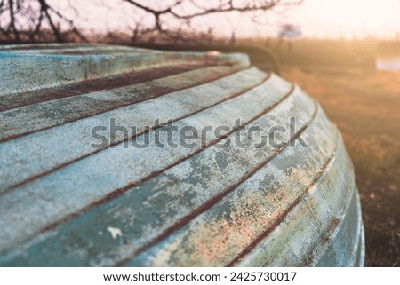 Close-up of the weathered, bluish surface of an old wooden boat on the shore in the light of the sunset.