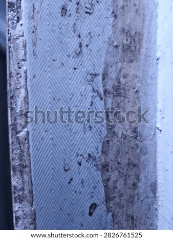 Close-up of a weathered chevron-patterned tile strip with dirt stains, alongside a rough concrete surface, showing aged and grungy texture
