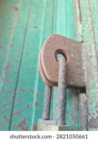 Close-up of a weathered, corroded padlock locking a rustic green metal rolling shutter or garage door, showing strong rust textures.