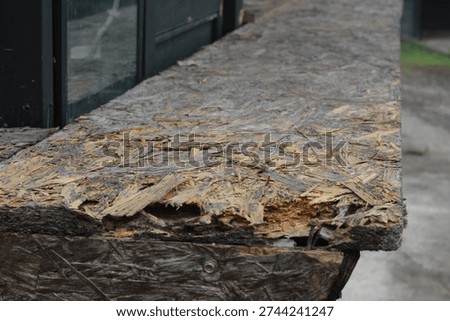 Close-up of a weathered and damaged Oriented Strand Board (OSB) wooden panel with visible splinters and decaying texture.