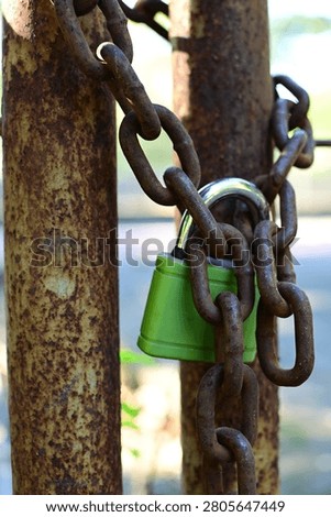 Close-up of a weathered green padlock securing a heavy rusted iron chain around corroded poles. Features shallow depth of field, high texture detail, and industrial security theme.
