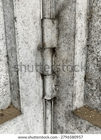 Close-up of weathered metal hinge with rust and dirt on gray textured panels