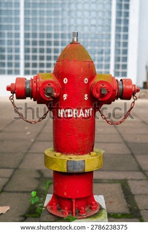 Close-up of a weathered red fire hydrant with metal chains standing on a tiled pedestrian walkway. A vital urban safety infrastructure detail. A classic red fire hydrant on a paved sidewalk.