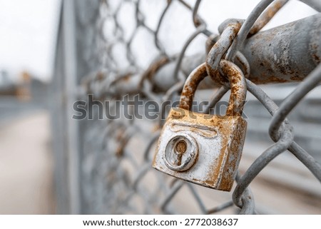 A close-up of a weathered, rusty padlock attached to a chain-link fence, symbolizing security and access restriction.