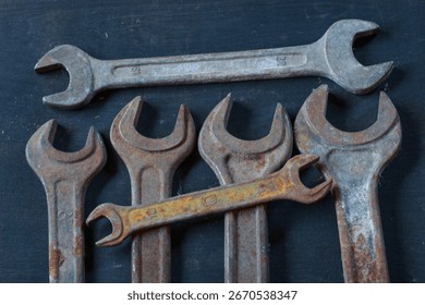 A close-up of weathered, rusty wrenches and a hook on a dark surface, showcasing their aged texture and industrial charm. Perfect for vintage tool enthusiasts.