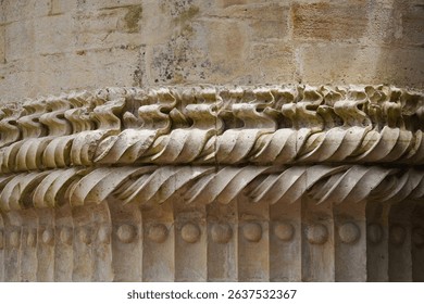 A close-up of weathered stone architecture. Intricate carvings adorn a cornice, showcasing detailed patterns and textures against a dark background.