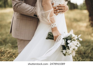 Close-up wedding couple bride and groom walk hand in hand through a pine forest, sunlight filtering through the trees, high lighting their joyful expressions.