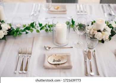 Close-up of a wedding dinner table. The inscription BRIDE on the shell in center of the table. Serving a table - knives, forks, glasses, wine glasses, candles, against background of gray tablecloth