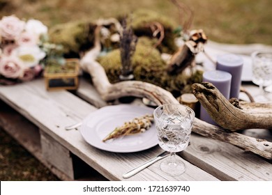 Close-up of a wedding dinner table. A table made of construction pallet decorated with driftwood and a car. The branches of the tree lie among plates and glasses. Wedding in Iceland