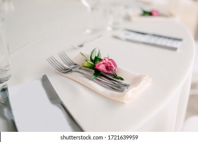 Close-up of a wedding dinner table. Serving a wedding table - forks lie on a napkin. The grooms bud is on the cutlery. Cream tablecloth on the round table