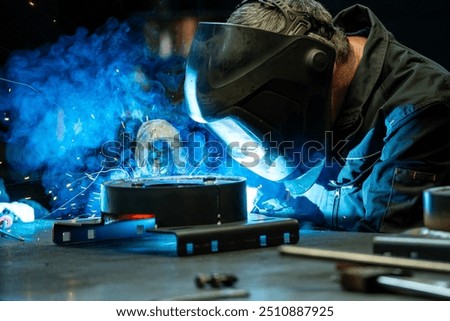 Close-up of a welder focused on his work, bright blue light and sparks emanating from the welding torch.