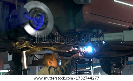 Close-up welding work on a lifted car. View from the back. Mechanic welds the bottom of the car.
