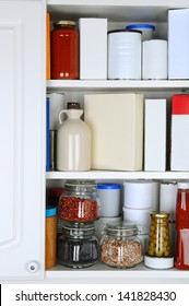 Closeup Of A Well Stocked Pantry. One Door Of The Cabinet Is Open Revealing Canned Goods, Condiments, Package Foodstuffs, And Storage Jars.