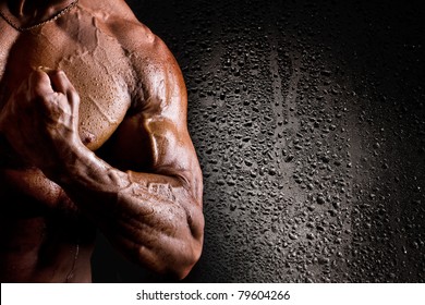Close-up of wet athletic torso and arm on black background with water drops