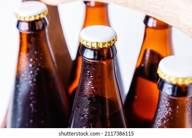 Close-up of wet six bottles necks of beer in a wooden case on a white background. Top view. Alcoholic drinks for the holiday.