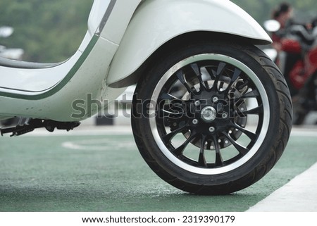 Close-up of wheels of a scooter motorcycle parked on a beautiful road in the daytime.	