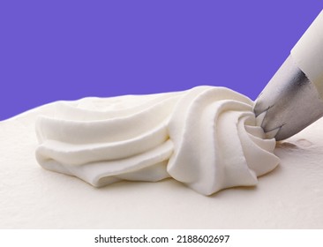 Closeup of whipped cream squeezed over a freshly white cake, Isolated on purple background - Shutterstock ID 2188602697