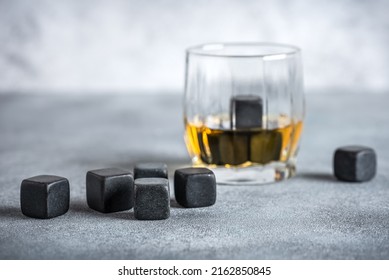 Closeup of whiskey stones and a glass of whiskey on a gray concrete table. Side view, selective focus.