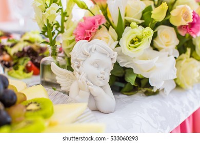 closeup white angel on table, on background of artificial flowers