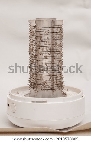 Close-up of a white bug zapper covered in dead mosquitoes. Shows effective pest management and insect bite prevention indoors.
