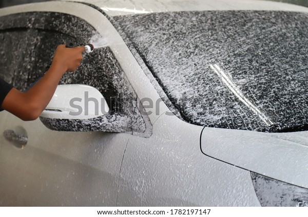 Closeup of white car cleaning, washing with high\
pressure foam spraying by male worker\'s hand before rubbing to\
remove dust and dirty\
things.