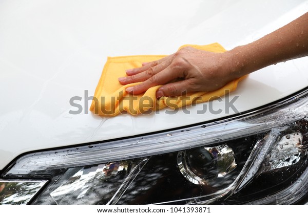 Closeup of white car cleaning  with yellow\
microfiber cloth by woman\'s hand in sunny\
day.