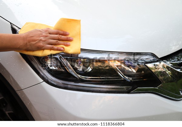 Closeup of white car cleaning  with yellow\
microfiber cloth by woman owner\'s hand in sunny day. The simply\
family activity and\
lifestyle.