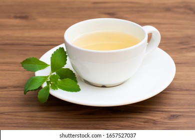 Closeup white ceramic cup of herbal tea with stevia leaves isolated on rustic wood table background.