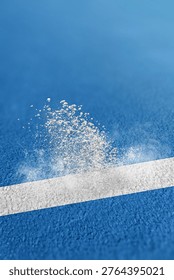 Close-up of white chalk powder exploding into the air as a tennis ball strikes the boundary line on a blue hard-court surface, capturing a precise sports moment