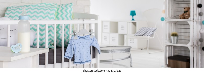 Close-up Of White Cradle With Pretty Pillows In Baby's Room. Next To It On Night Stand Bottle With Milk And Teat