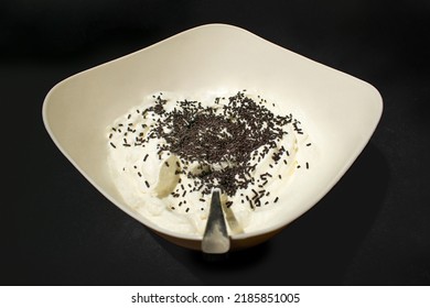 Close-up Of White Cream Filling With Chocolate Sprinkles Whisked In A Bowl On Black Background. Black And White Aesthetic. Process Of Making Birthday Cheesecake.