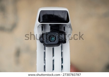 Close-up of a white drone's camera module with a black lens housing mounted on a textured surface showing the device's compact design for aerial photography or videography in outdoor environments.