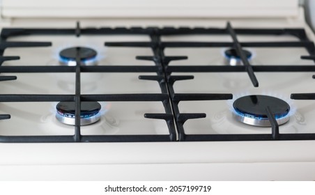 Close-up of a white enameled gas stove with black burners burning with blue fire. Cast-iron grates for kitchen utensils