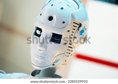 Closeup of white illuminated human robot winks looking camera against blurred background