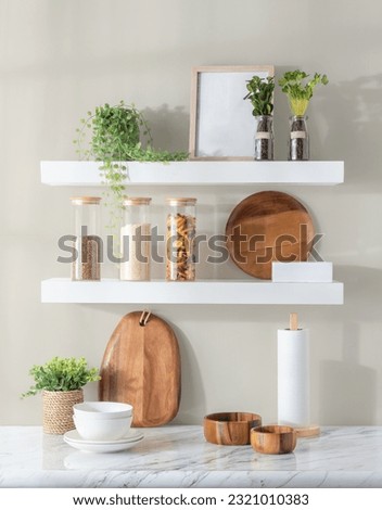A close-up of a white kitchen countertop with various items such as dishes, plants and decorative objects displayed on an open shelf