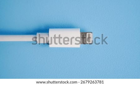 Close-up of a white Lightning cable for Apple devices on a light blue background, showing detailed connector design with studio lighting