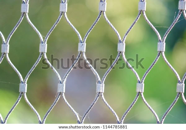 Close-up of the\
white metallic mesh that have some spider web, with blurred\
defocused natural green as\
background.