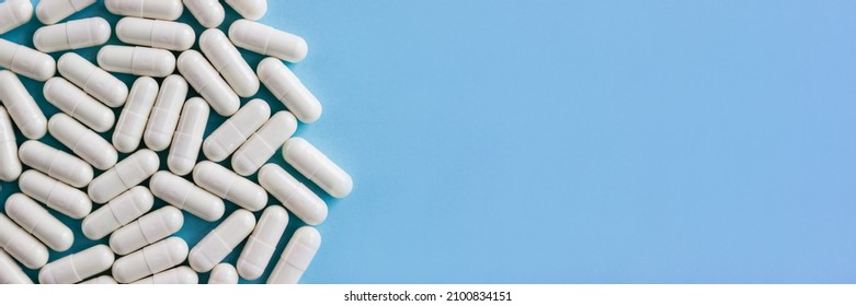 Close-up white pharmaceutical pills with colostrum on blue background. Horizontal banner, selective focus, copy space