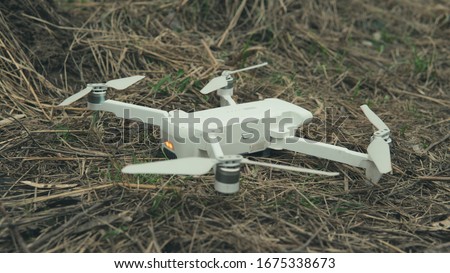 Close-up of white quadrocopter on ground in grass. Modern drone unmanned aerial vehicle with propellers.
