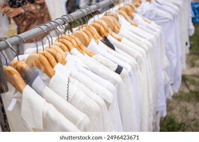 Close-up of white shirts hanging on wooden hangers outdoors. Fashionable, minimalist clothing display at an outdoor market or fair. - Powered by Shutterstock