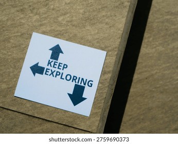 Close-up of a white sticker with 'KEEP EXPLORING' and arrows on cardboard background