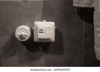 Close-up of a white temperature controller and valve on gray tiled bathroom wall. Modern heating system detail showing minimalistic design, comfort, and smart home functionality