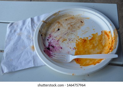 Closeup Of White Used Dirty Heavy Duty Paper Plate With Orange And Purple Stains And Used White Napkin Plastic Fork On White Table